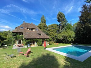 Una casa con piscina, un patio con sillas y un jardín.