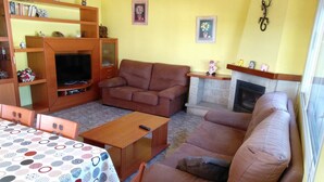 Una sala de estar acogedora con un sofá marrón, un mueble de entretenimiento de madera, una mesa de comedor con mantel estampado y una chimenea.