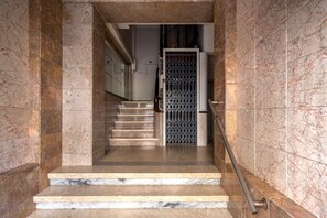 Un escalier en marbre menant à une porte surmontée d’un portail en métal.