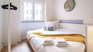 Een slaapkamer met een bed, een raam, een wandklok en een kapstok.