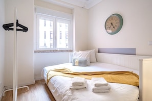A bedroom with a bed, a window, a wall clock, and a coat rack.