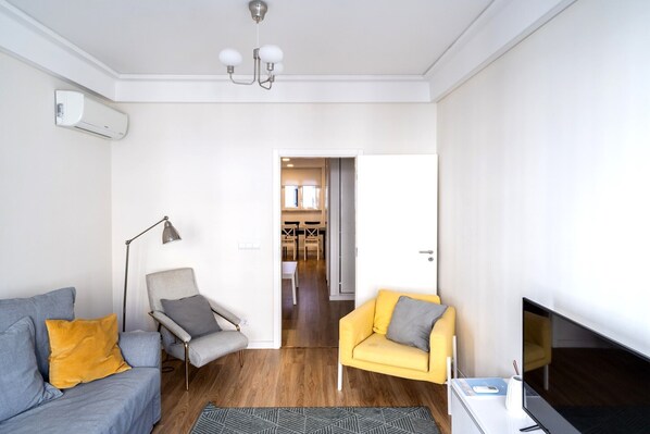 Un salon moderne avec un canapé gris, un fauteuil jaune, une lampe sur pied et un téléviseur à écran plat.