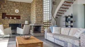 Una sala de estar con chimenea de piedra, una mesa de centro de madera, un sofá con cojines estampados, una estantería y una escalera en espiral.