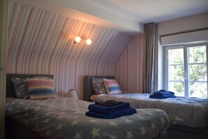 A bedroom with two beds, striped wallpaper, a window, and a ceiling light fixture.