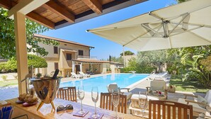 Un bar a bordo piscina con vista sulla piscina, poltrone relax e una zona patio coperta.