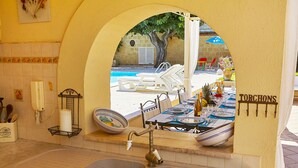 Una cucina con lavandino, una finestra vista piscina e lettini, e un cartello con la scritta 'TORCHONS'.