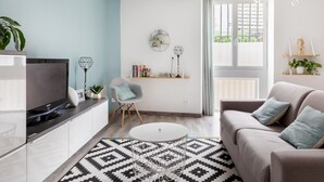A modern living room with a TV, sofa, and coffee table. There are shelves with books and decorative items, and a window with curtains. - La maison de Valentine *** (Bordeaux)