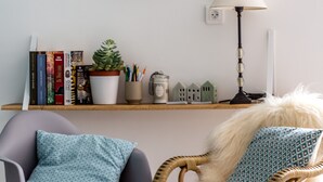 A room with a grey armchair, a wicker chair with a fluffy white cushion, a metal shelf with plants and books, and a lamp. - La maison de Valentine *** (Bordeaux)