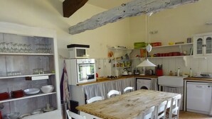A kitchen with white cabinets, a wooden table, and chairs. There is a microwave, oven, and washing machine.
