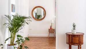 A room with a wooden herringbone floor, a round mirror on the wall, a small wooden side table with a lamp, and a potted plant. - Art Filled Apartment in the Heart of Riga (Riga)