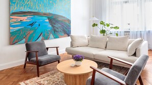 A modern living room with a large abstract painting, a beige sofa, two armchairs, a round wooden coffee table, and a potted plant. - Art Filled Apartment in the Heart of Riga (Riga)