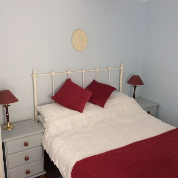 A bed with a white headboard, two red pillows, and a white blanket. There are two bedside tables with lamps and a small round mirror on the wall.