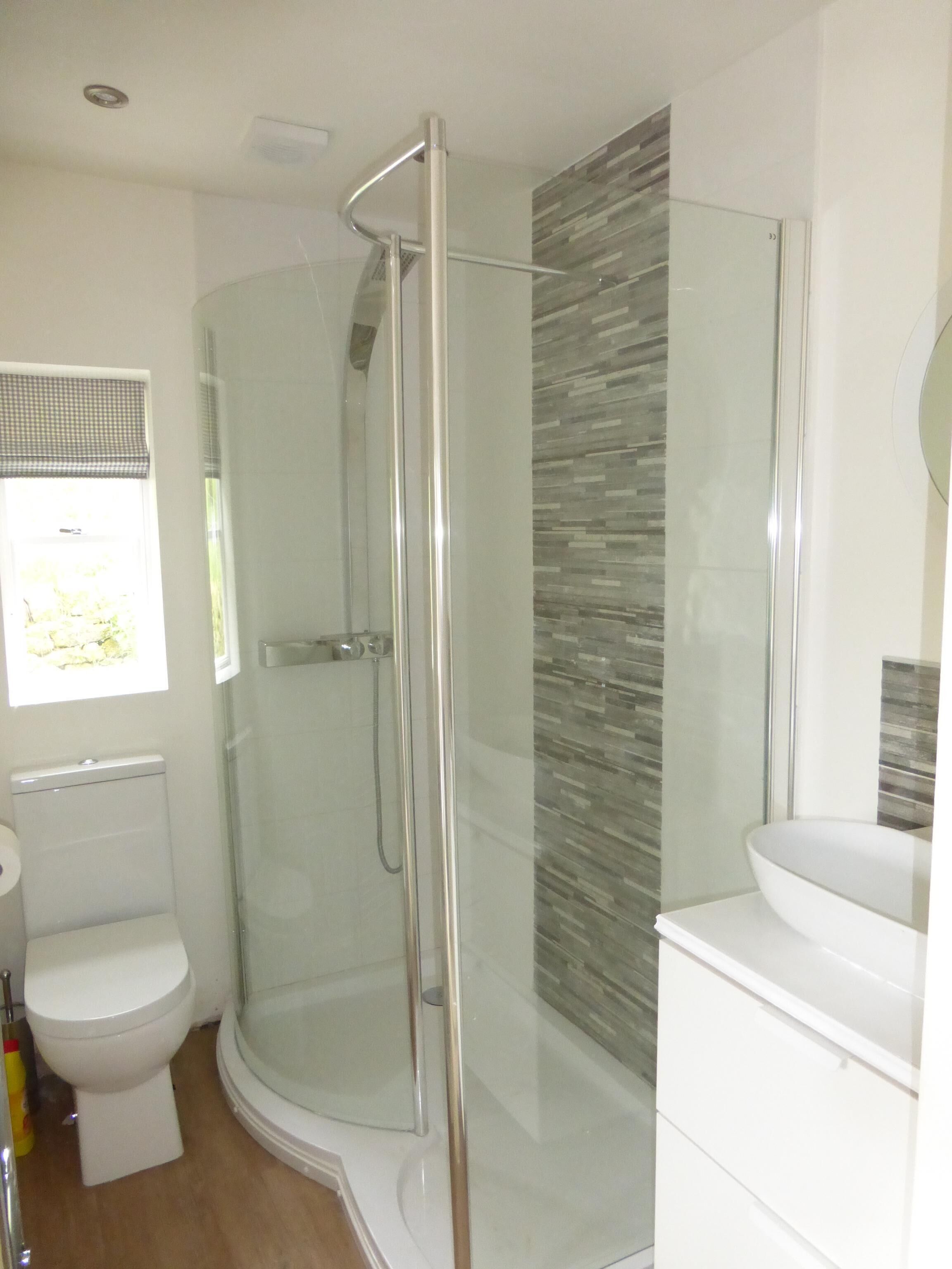 A modern bathroom with a glass-enclosed shower, a toilet, and a sink with a mirror.