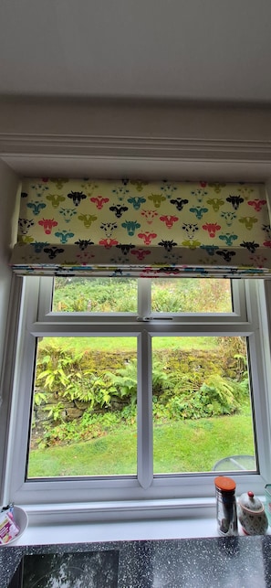 A window with a patterned valance, a stone wall, and a grassy garden view.