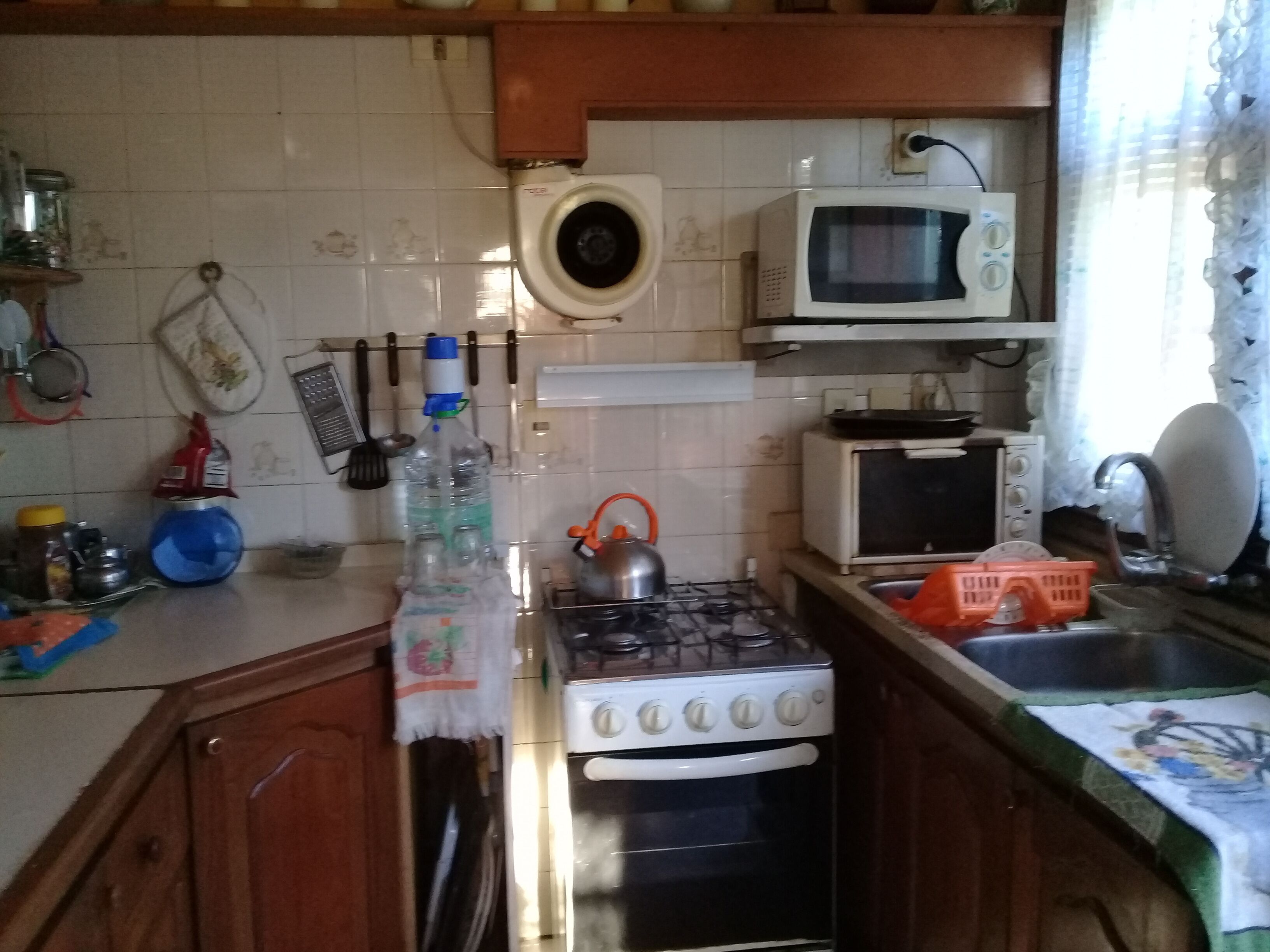 A kitchen with a gas stove, a microwave, and a sink. There are various kitchen utensils and bottles on the counter.