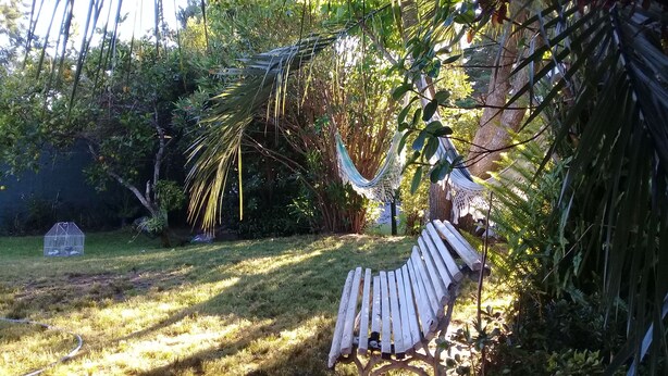 Eine Hängematte unter einem Baum, eine hölzerne Bank und ein Vogelkäfig in einem Garten.