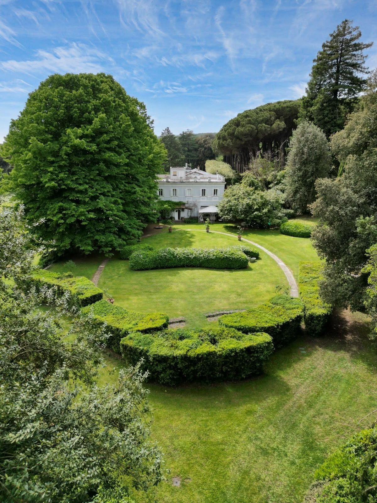 A large, well-maintained garden with a central lawn, surrounded by neatly trimmed hedges and trees.