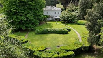 A large, well-maintained garden with a central lawn, surrounded by neatly trimmed hedges and trees.