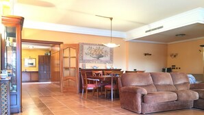 A spacious living room with a brown leather sofa, a dining area with wooden furniture, and a large painting on the wall. - Villa Mercè. Golden Coast (Botarell)