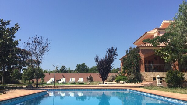A clear blue pool with lounge chairs, surrounded by trees and a building with a tiled roof. - Villa Mercè. Golden Coast (Botarell)