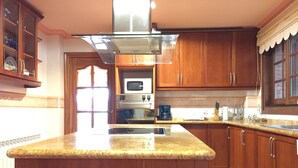 A kitchen with wooden cabinets, a granite countertop, a stainless steel range hood, a microwave, and a coffee maker. - Villa Mercè. Golden Coast (Botarell)