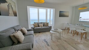 A living room with a grey sofa, a small round table, and a dining area with white chairs.