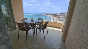 Un balcón con mesa y sillas, con vistas a una playa y al paisaje urbano.