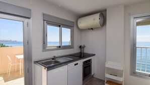 A compact kitchen with a dishwasher, oven, and a window overlooking the sea.