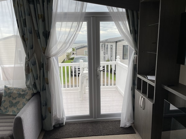 Une pièce dotée d’une porte-fenêtre coulissante donnant sur un balcon avec une balustrade blanche, d’où l’on peut admirer des maisons et une voiture garée à l’extérieur.