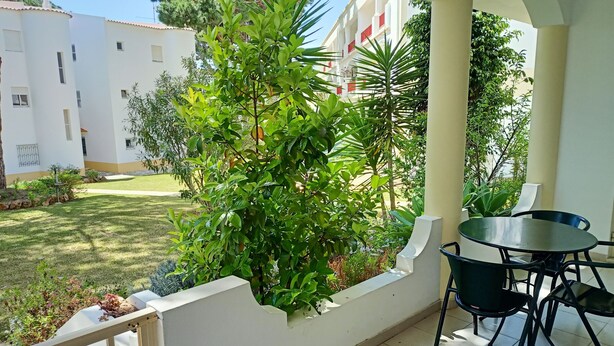 Un balcon avec une table et des chaises, entouré de verdure et offrant une vue sur les bâtiments.