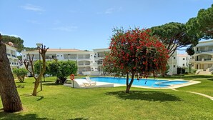 Un espace piscine avec un arbre et un bâtiment blanc en arrière-plan.