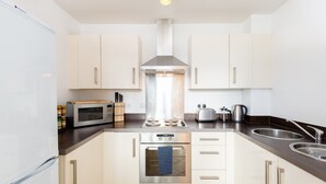 A modern kitchen with white cabinets, stainless steel appliances, and a central range hood. - Skyline Birmingham City Centre Penthouse (Birmingham)