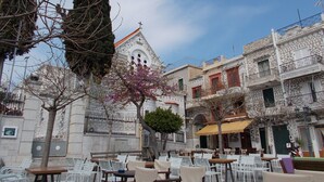 An outdoor cafe area with white plastic chairs and tables, surrounded by buildings with intricate geometric patterns and balconies.