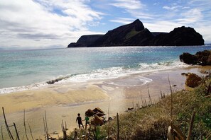 A beach with clear water, a rocky outcrop, and two people walking.
