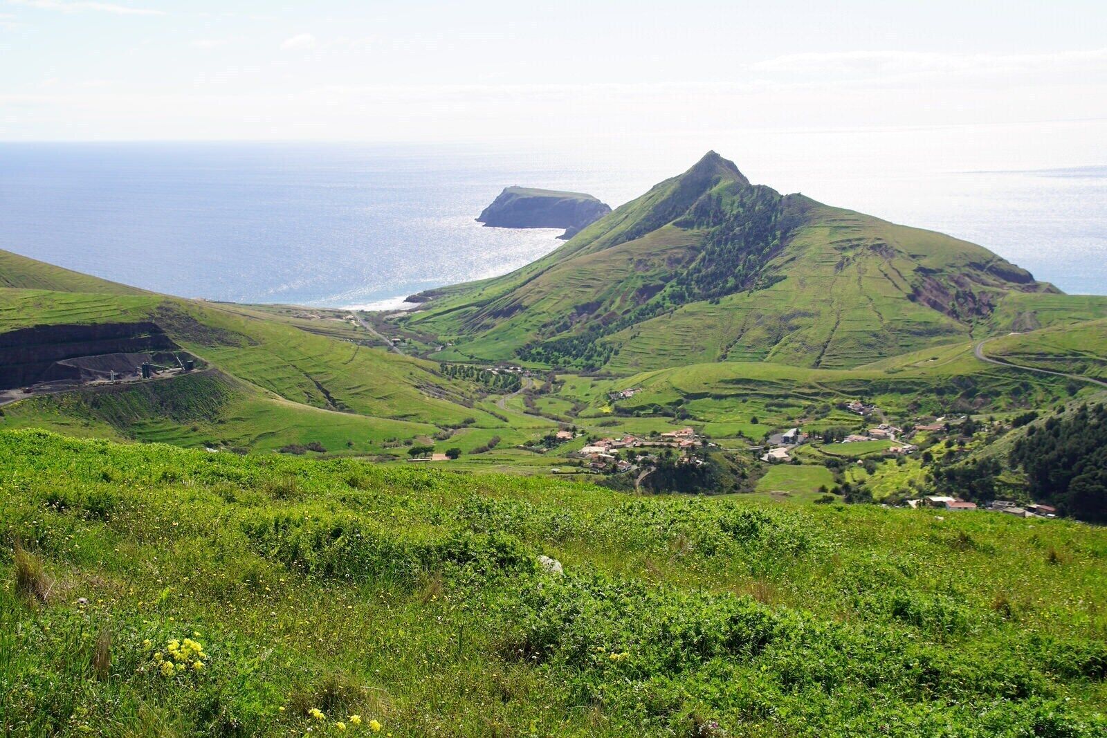 A coastal landscape with rolling hills, a small settlement, and a prominent mountain peak.