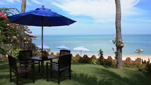 Une terrasse avec une table et des chaises, un parasol bleu et une vue sur l’océan.