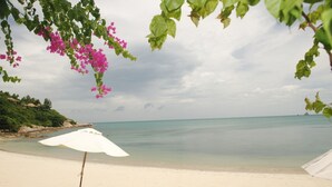 Une plage avec un parasol blanc et deux chaises longues.