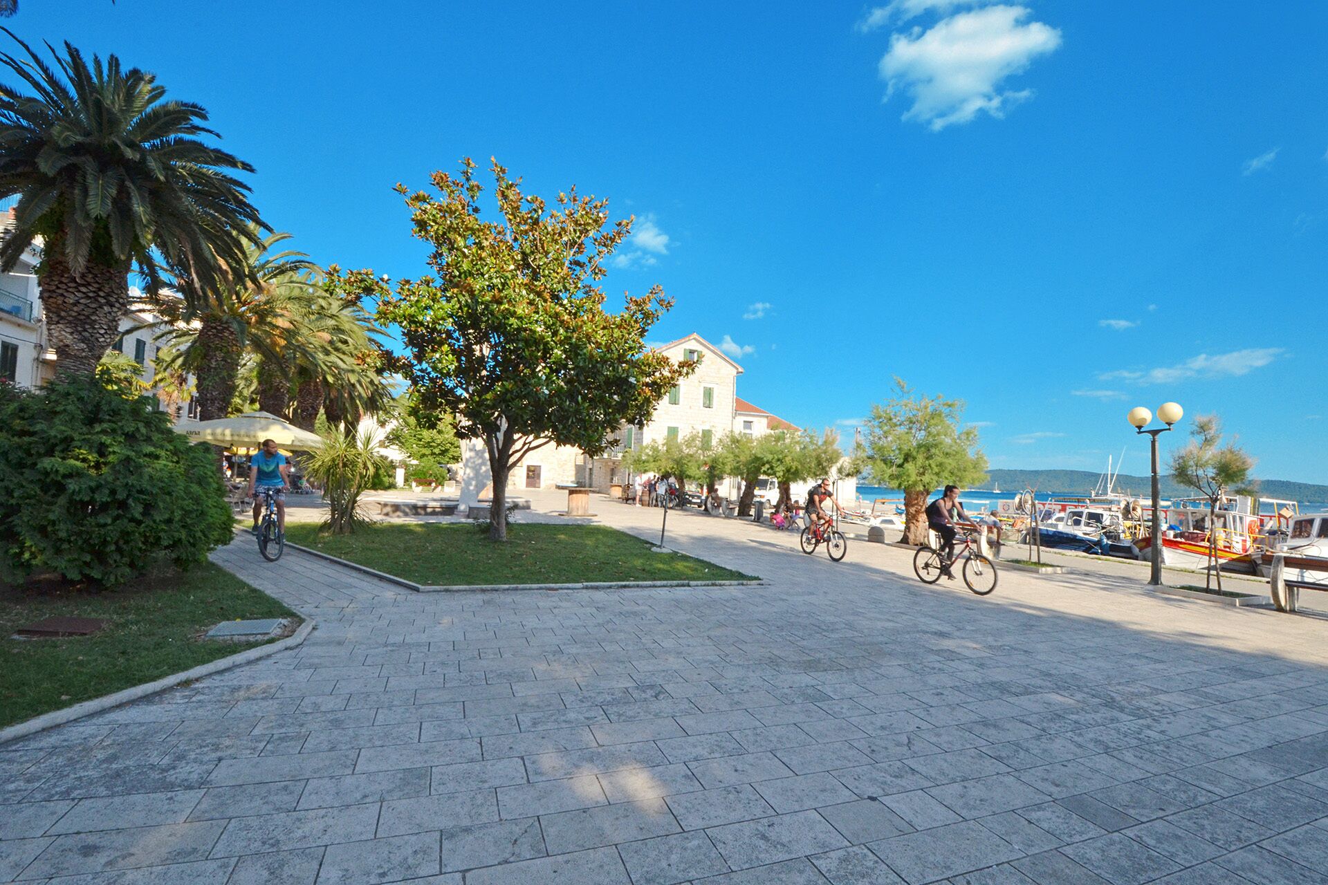 Ein gepflasterter Fußweg mit einem Baum, einem Gebäude und Blick aufs Meer.