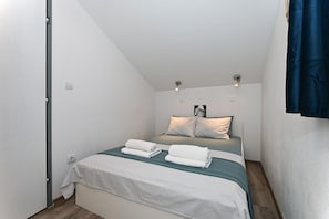 Ein kleines, modernes Schlafzimmer mit einem Bett, zwei Nachttischen, einer Wandleuchte und einem Fenster mit Vorhang.