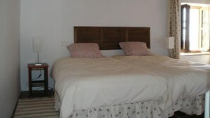A bedroom with a wooden headboard, two beds with striped pillows, a bedside table with a lamp, and a window with curtains. - Casa Ábalos, in the middle of nature (Periana)
