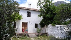 A white building with a tiled roof, a wooden door, and a stone wall. - Casa Ábalos, in the middle of nature (Periana)