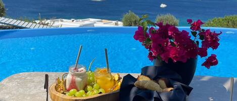 A table with food and drinks by a pool with a view of the sea.