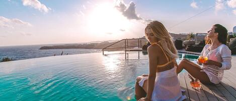 Um casal sentado à beira da piscina com vista para o pôr do sol.
