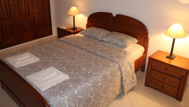 Un letto ben rifatto con una coperta a fantasia, due comodini con lampade e un armadio in legno.