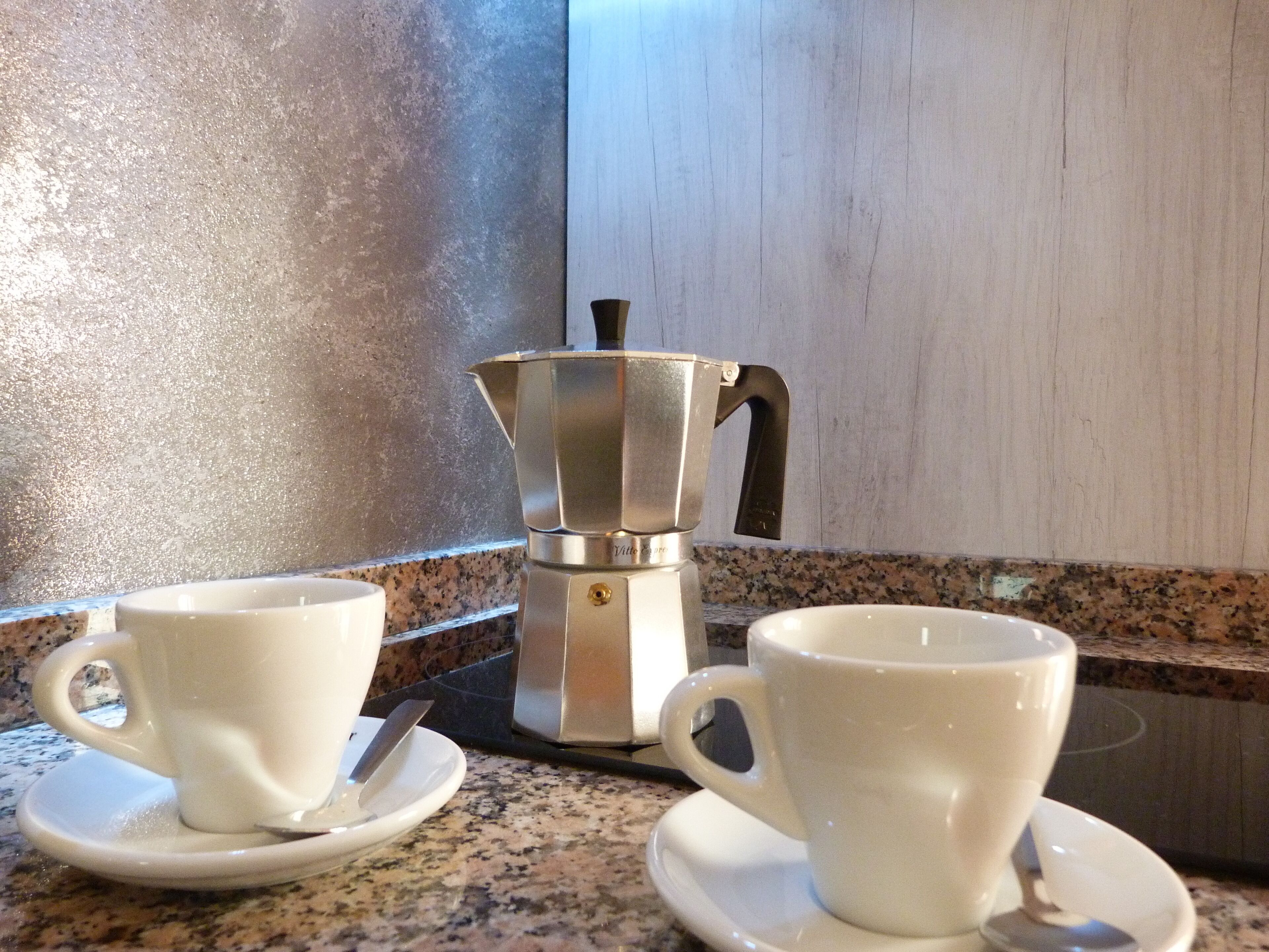 Une machine à café posée sur un plan de travail en granit, avec deux tasses et sous-tasses blanches.