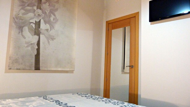 A bedroom with a bed, a wall-mounted TV, and a door.