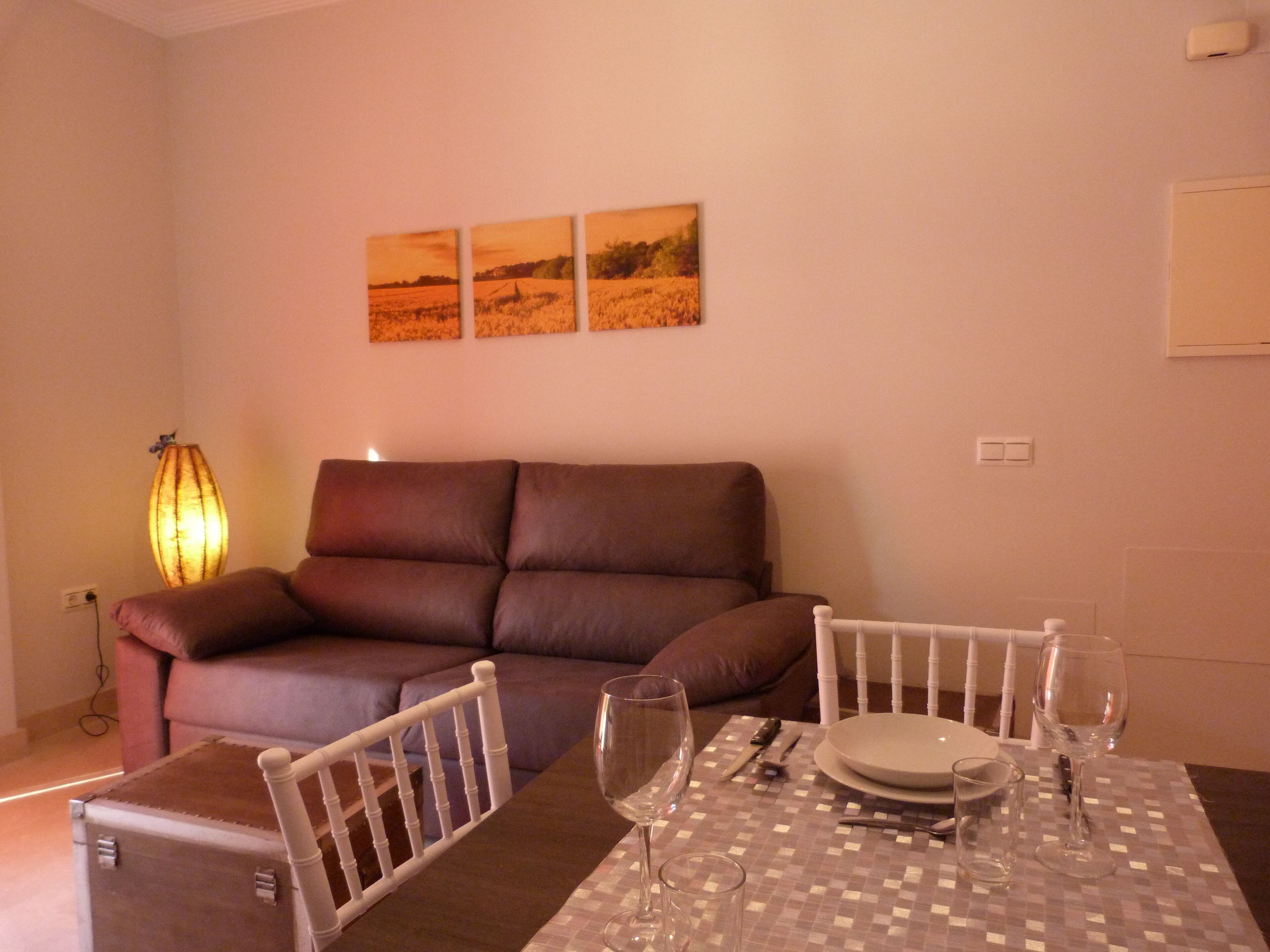 Ein Essbereich mit Tisch für zwei Personen, einer braunen Couch und einer Lampe.