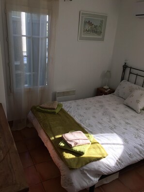 Et soveværelse med en seng, et natbord, en lampe, et vindue med gardiner og et billede i ramme på væggen.