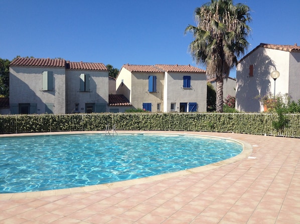 A swimming pool with tiled flooring, surrounded by buildings with red-tiled roofs and blue shutters.
