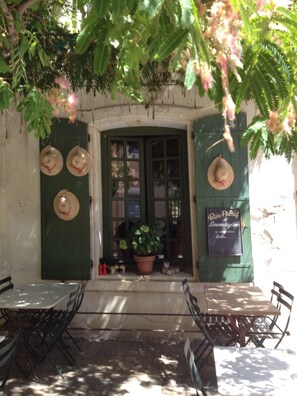 A café with outdoor seating, a green door, and hanging hats.